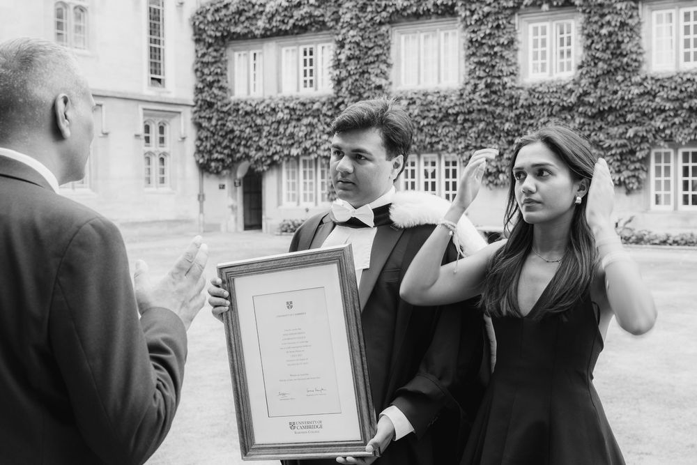 A vintage black and white photograph showing people at a graduation ceremony holding a framed certificate outdoors.