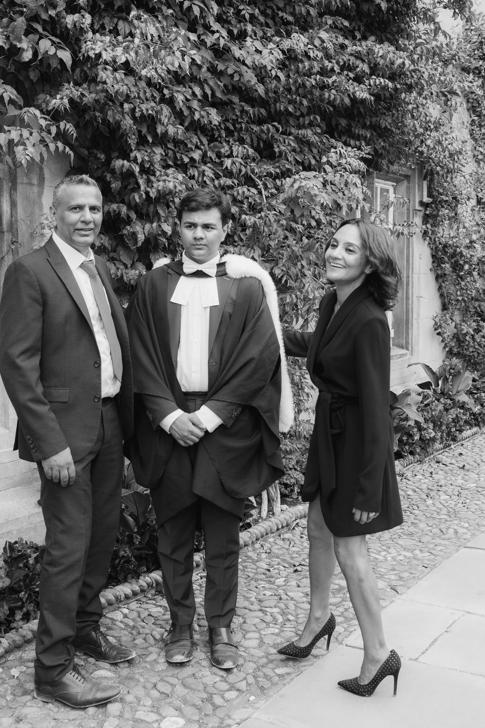 A series of four black and white photos showing people in formal attire posing against a cobblestone wall outdoors.