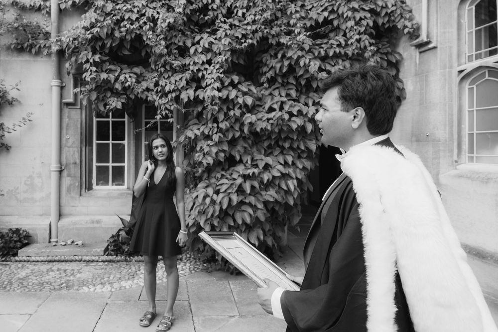 Black and white photo of students in academic robes standing outside a vine-covered building on campus.