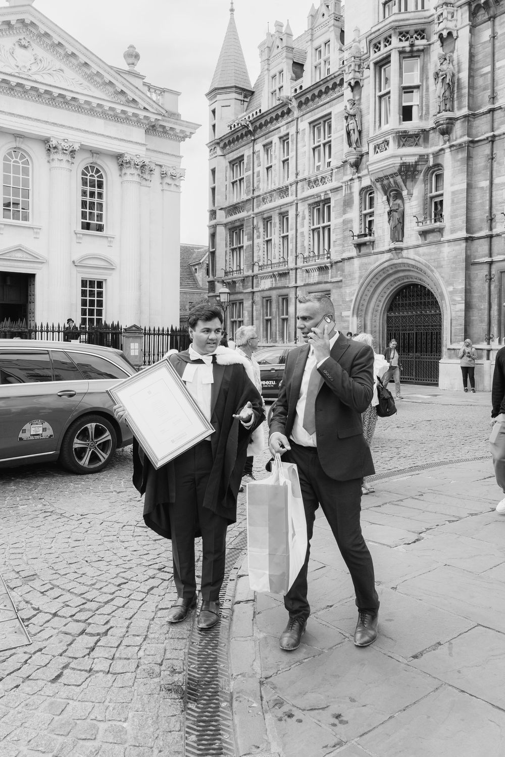 Two business professionals walking on a cobblestone street in Cambridge with historic university buildings in the background.
