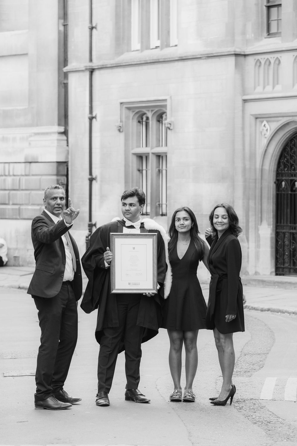 A black and white photo of a group standing outside a building celebrating with a framed certificate.