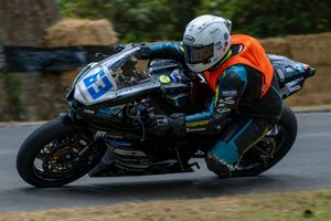 Motorcycle racer leaning into a sharp corner on a black sport bike during a road race competition.