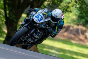 Motorcycle racer number 93 leaning into a curve on a racing bike at a tree-lined circuit track.