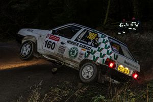 Skoda rally car number 160 cornering aggressively on a night forest rally stage.