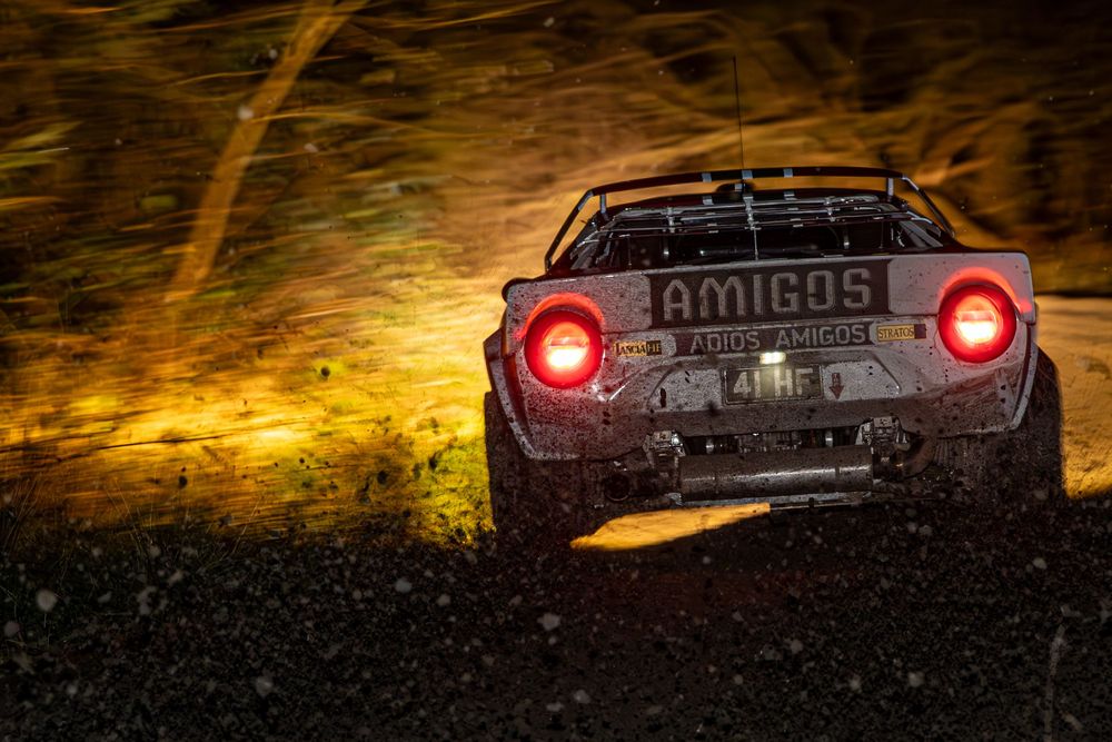 Amigos rally car kicking up dust and debris under dramatic golden night stage lighting.