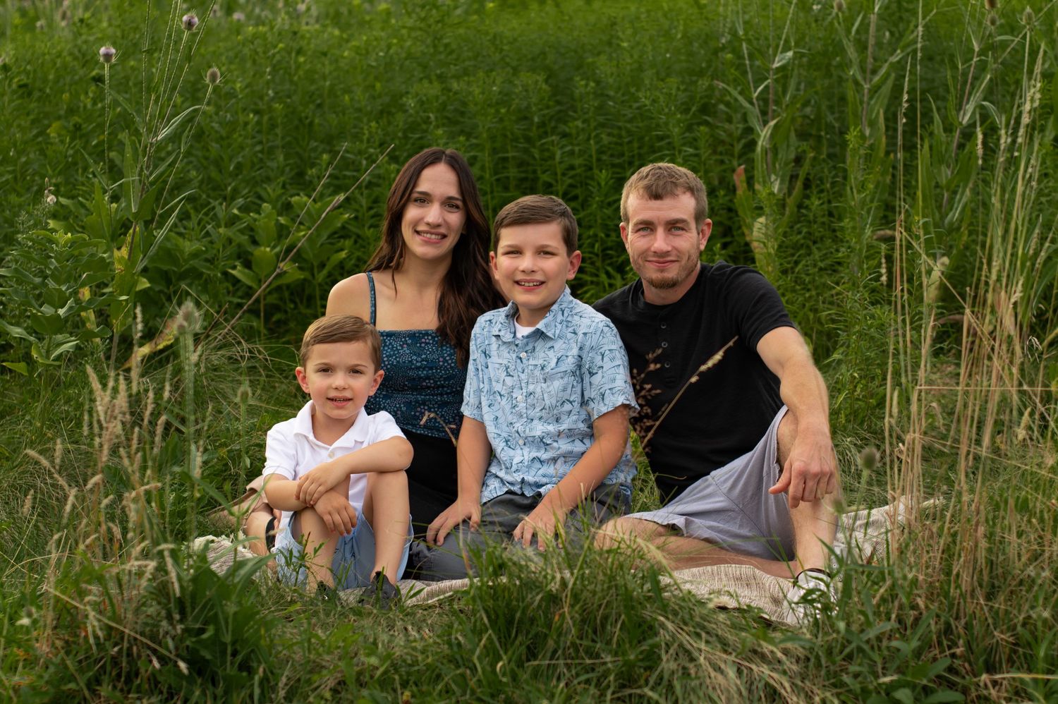 A family of four sits together on grassy hill during golden hour outdoors in summer.