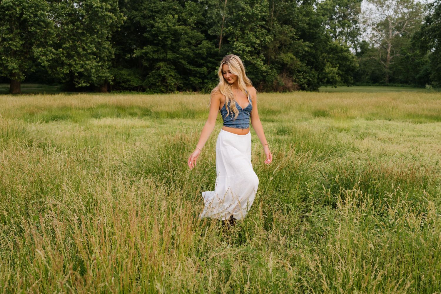 A person in a white summer dress walking through a tall grass meadow in warm sunlight.