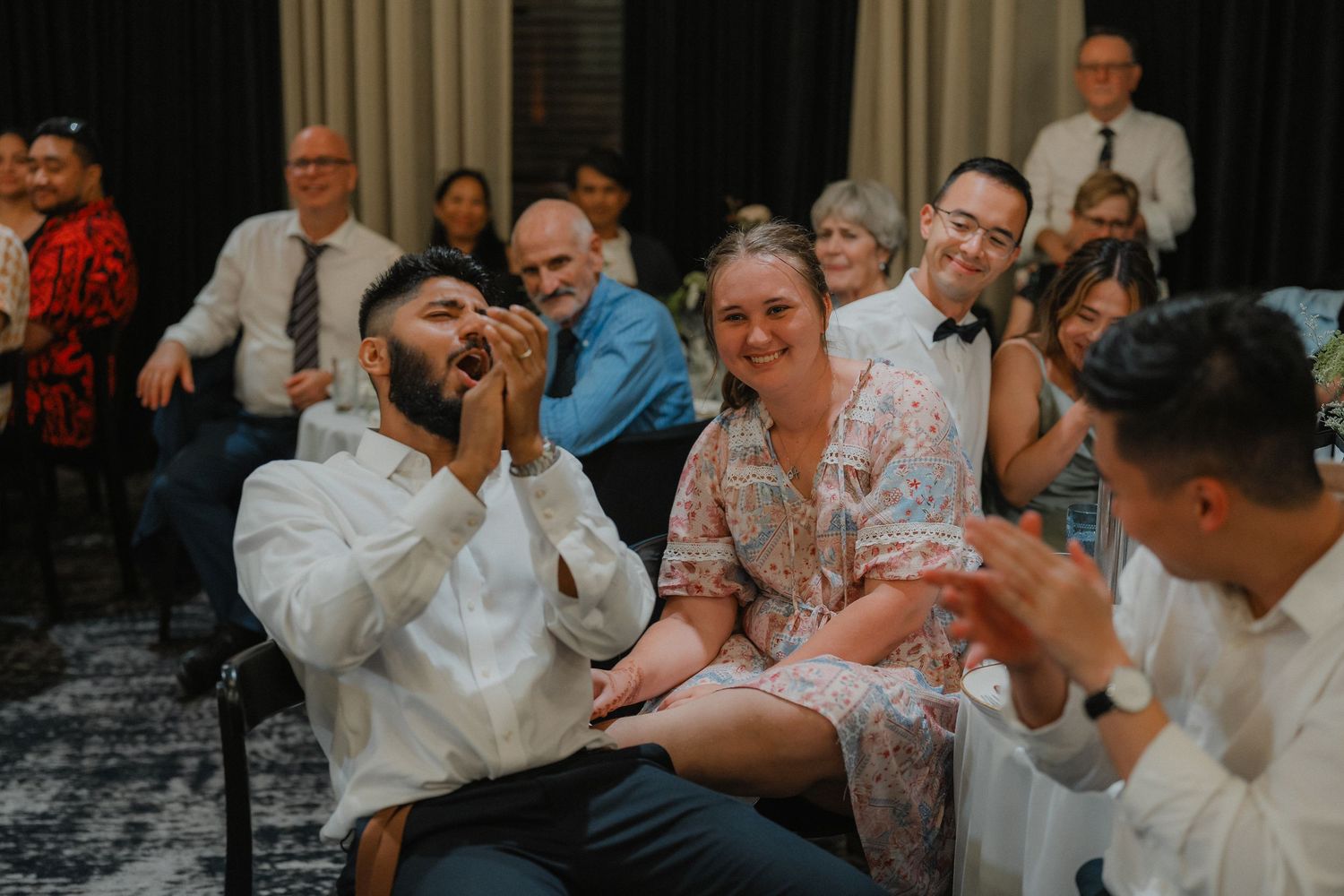 Guests at a wedding reception react with joy and laughter during a celebratory moment.