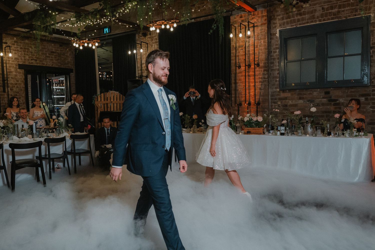 Groom walks through low-lying fog during wedding reception first dance.