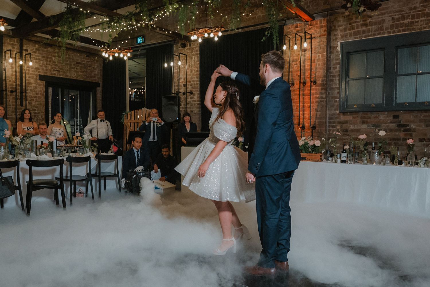 Couple sharing their first dance surrounded by fog effects on an industrial-style wedding venue dance floor.