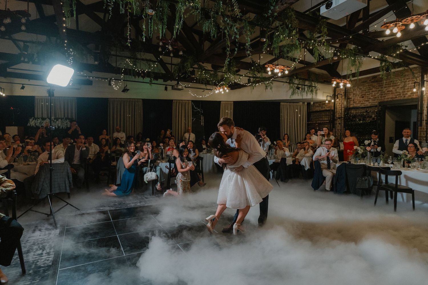 Wedding reception dance floor filled with fog as guests watch from the sides.