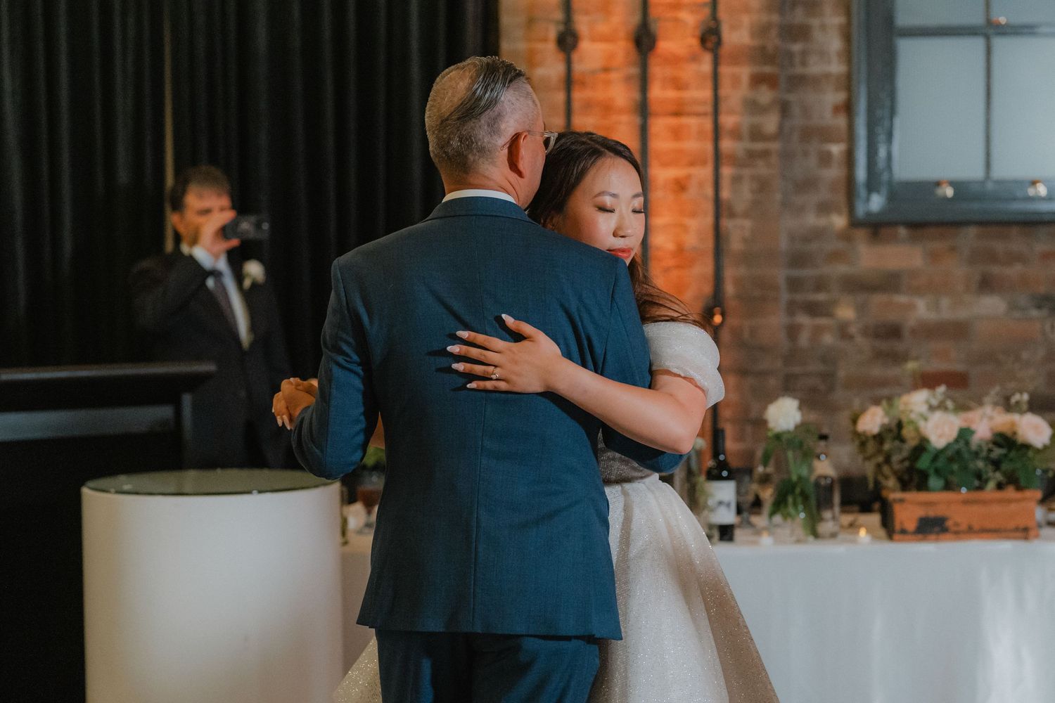 Intimate dance moment during wedding reception in industrial-style venue with exposed brick walls.