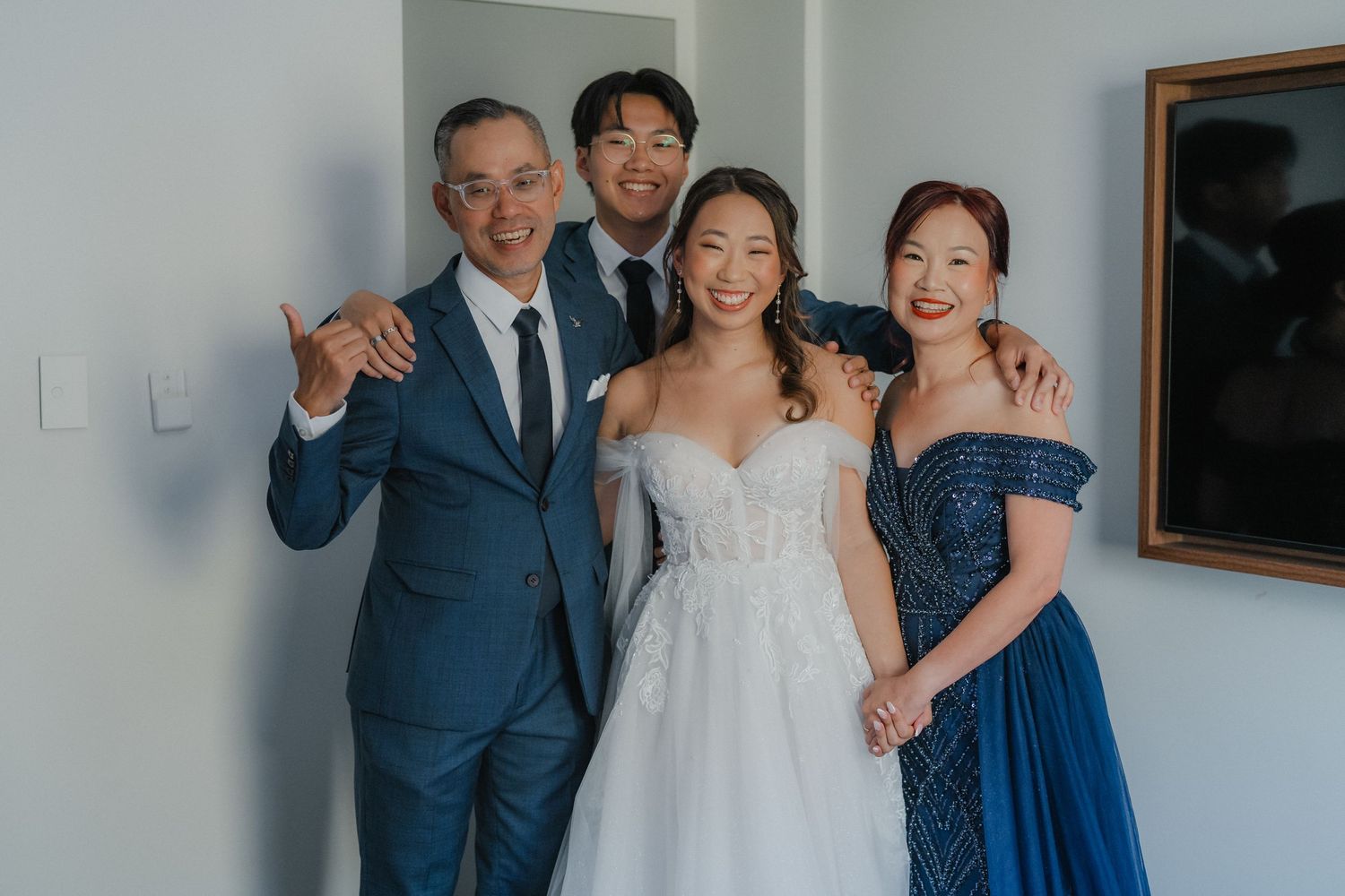 Wedding party members in navy suits and formal dresses gather for indoor group photos at a celebration.