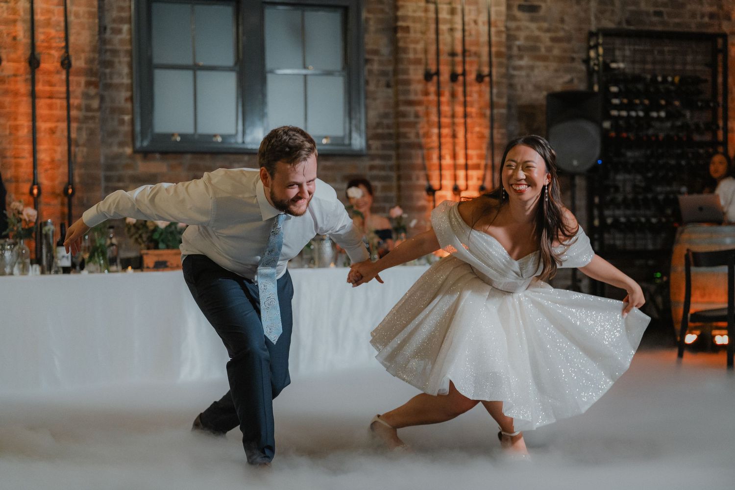 Dancing guests enjoying a fog-filled wedding reception in an industrial space with mood lighting.