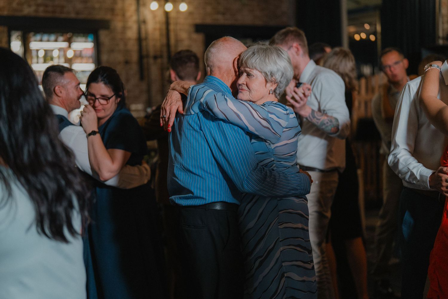 Couples dancing together during an evening wedding reception in a rustic brick venue.