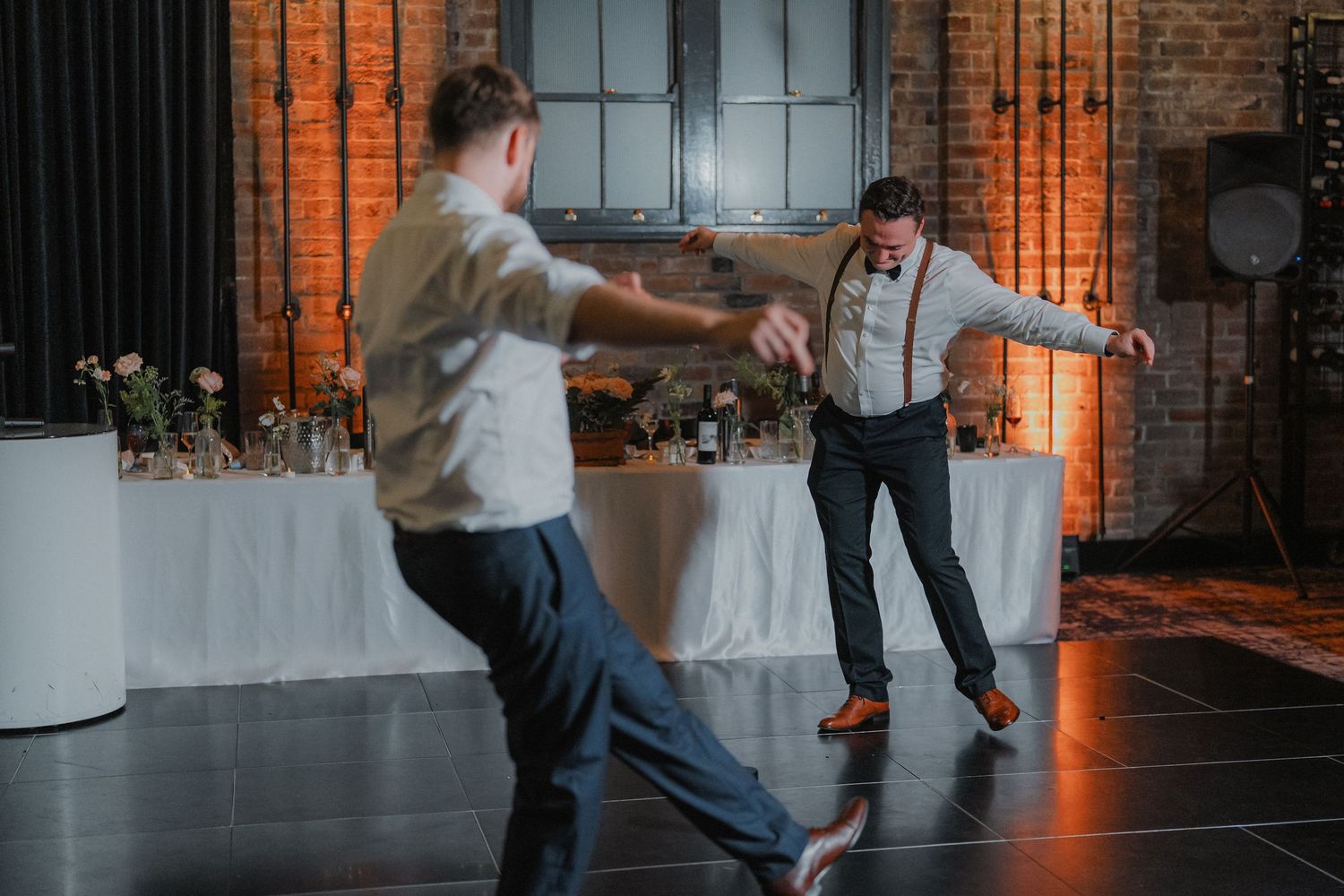 Dancers move energetically across a wedding reception floor in an industrial-style venue.