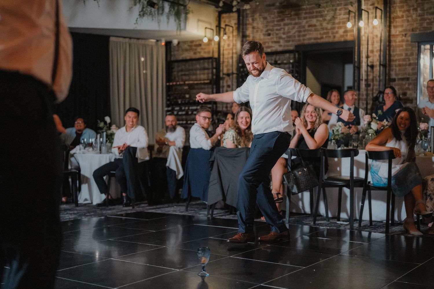 Wedding guests dancing and socializing on dance floor in atmospheric brick venue.