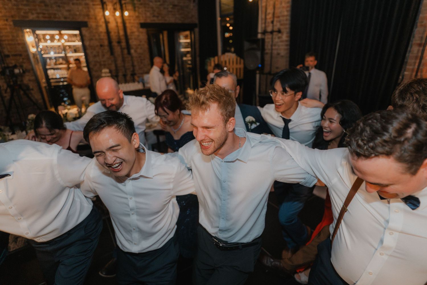 People dancing and laughing together at a lively wedding party in an industrial brick venue.