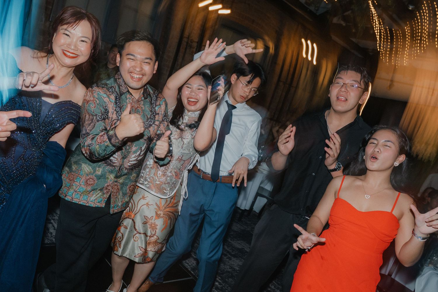Group of wedding guests posing and celebrating together at a dimly lit reception venue.