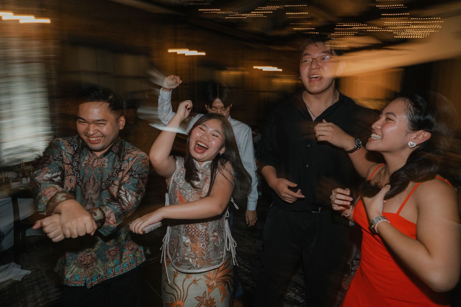 Wedding guests enjoying themselves on a dimly lit dance floor with dynamic movement and energy.