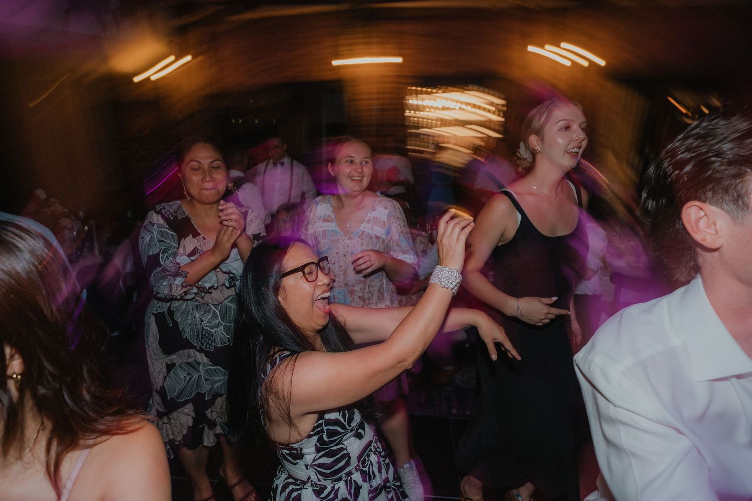 Energetic dancing continues at a wedding reception with colorful purple lighting effects.