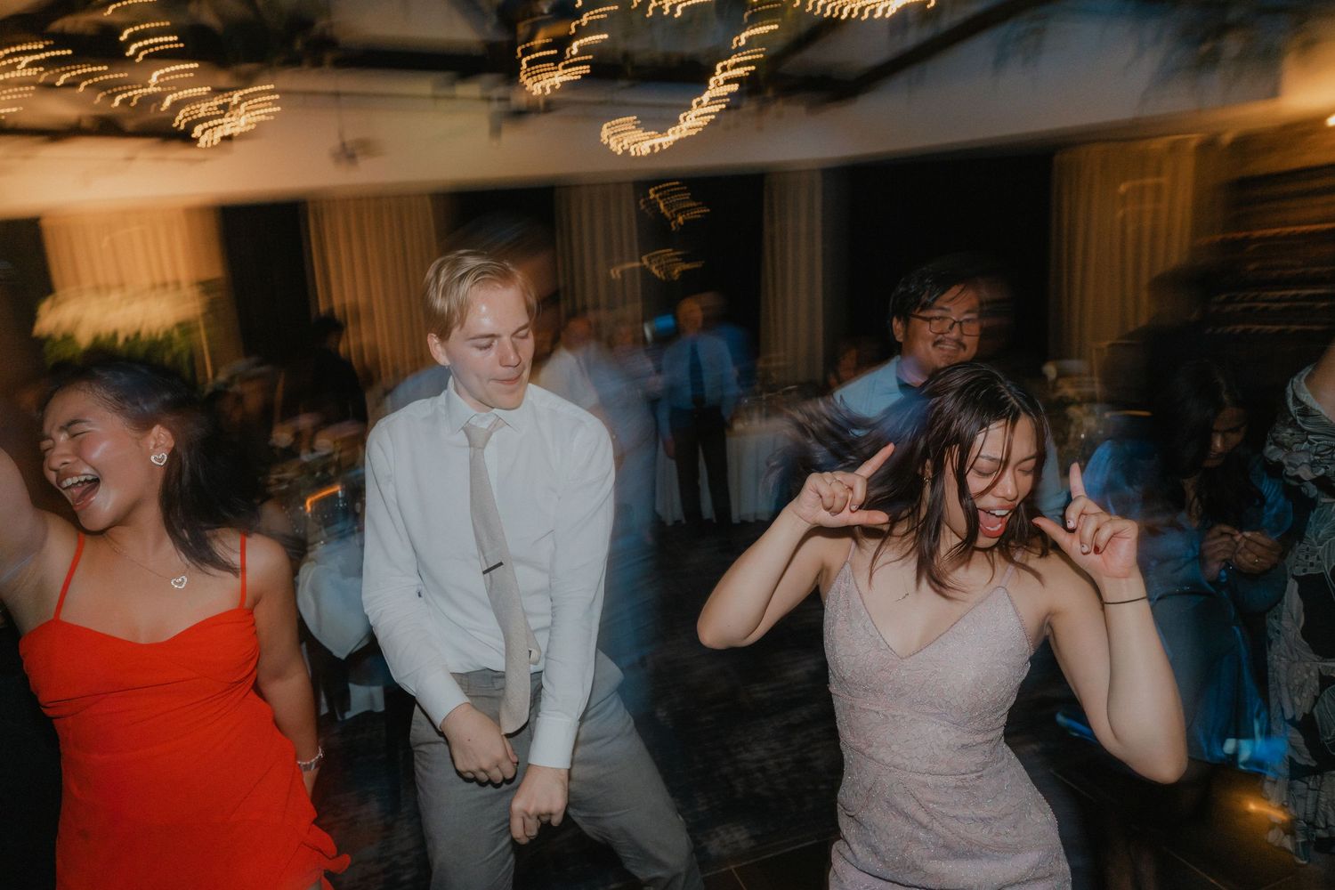Wedding guests dance enthusiastically on a crowded dance floor during a lively reception celebration.