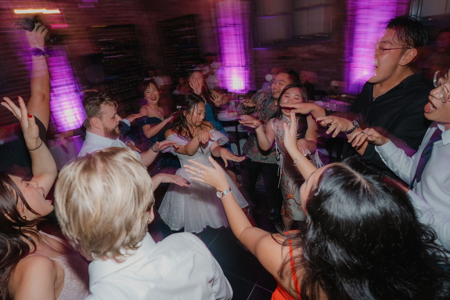 Dancing crowd celebrating at a nightclub with purple lighting and hands raised in excitement on the dance floor.
