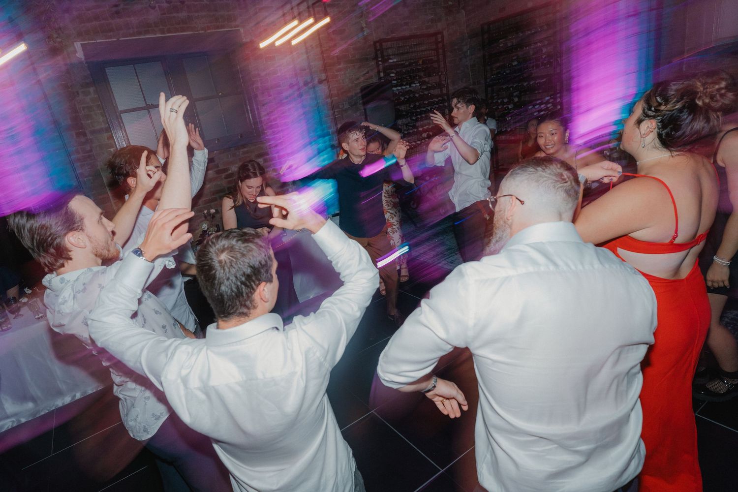 Energetic dance party with guests celebrating on illuminated dance floor under purple lighting.