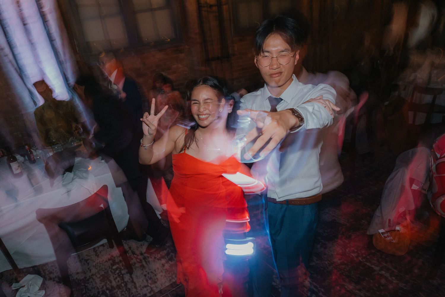 Party guests dancing and posing in dimly lit venue with red lighting effects.
