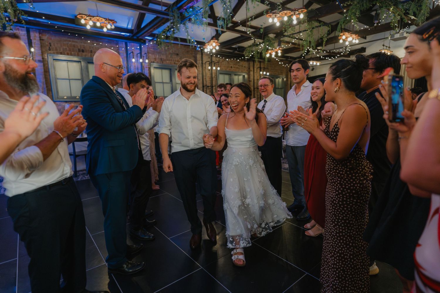 Wedding guests dancing together and celebrating on a crowded dance floor at an evening reception.
