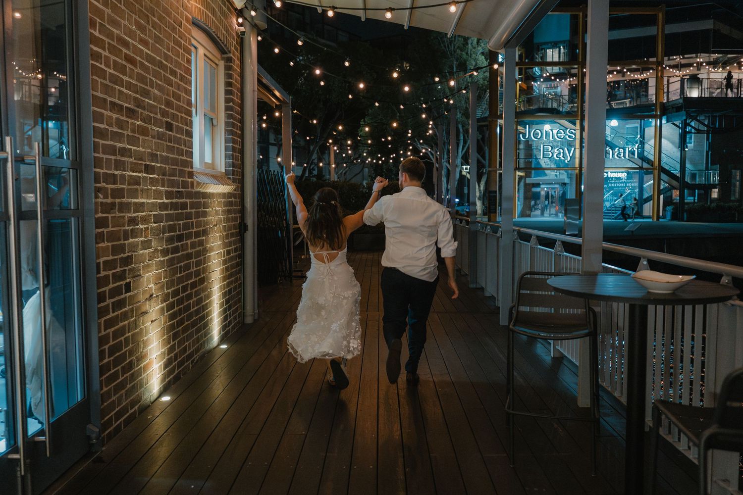 Wedding reception venue with exposed brick walls illuminated by string lights and blue ambient lighting.