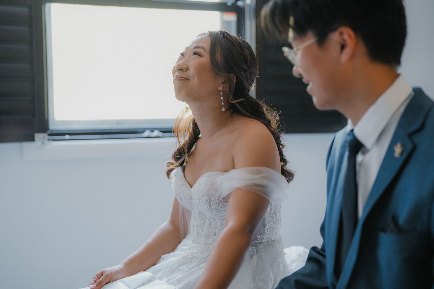 Bride and groom share a joyful laugh together during their wedding photoshoot in a bright indoor setting.