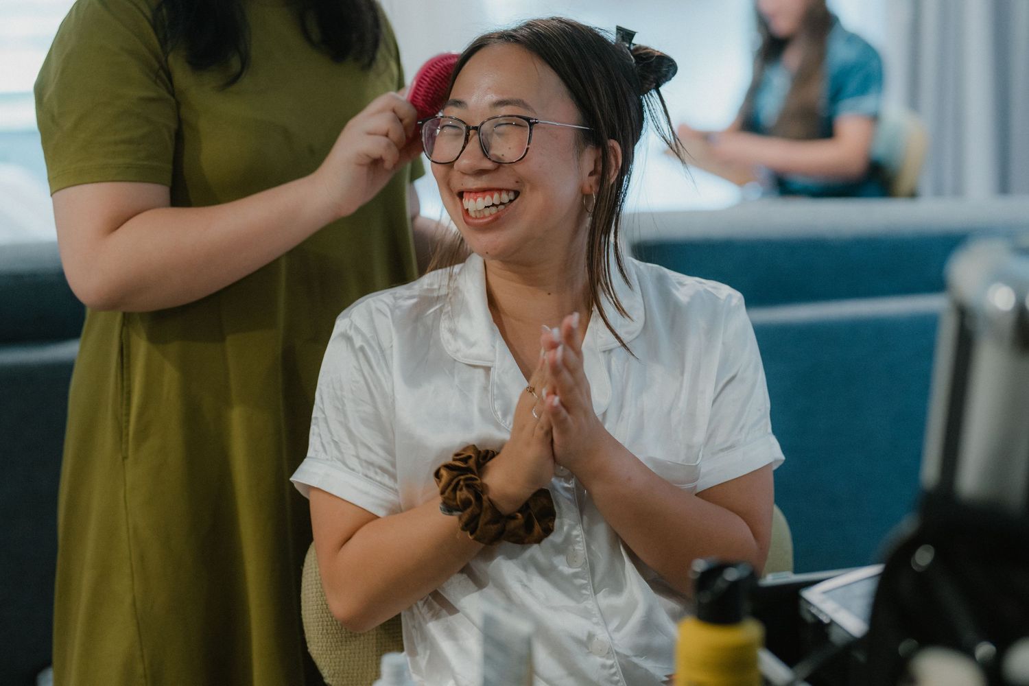 A person in a white shirt smiles brightly while getting their hair styled in a salon setting.