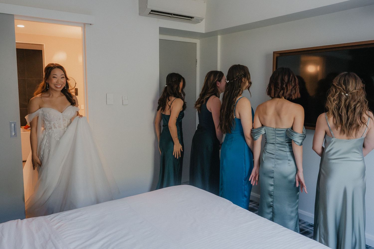A group of bridesmaids in light blue dresses seen from behind as they walk down a hallway.