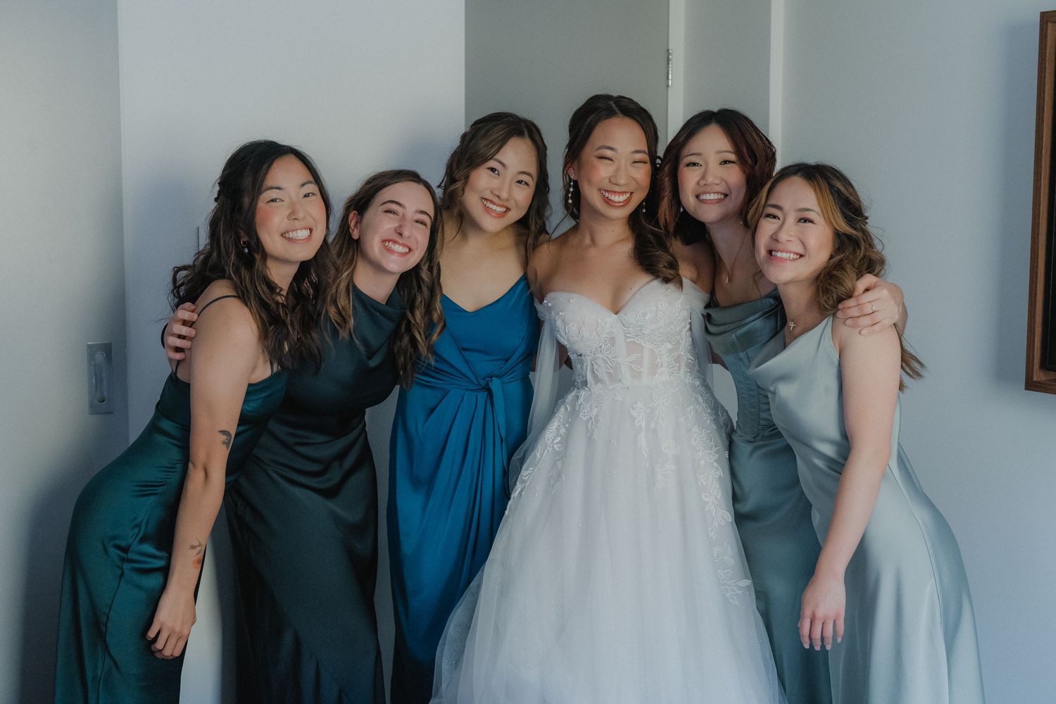 Wedding party in coordinating blue dresses poses together for a group photo.