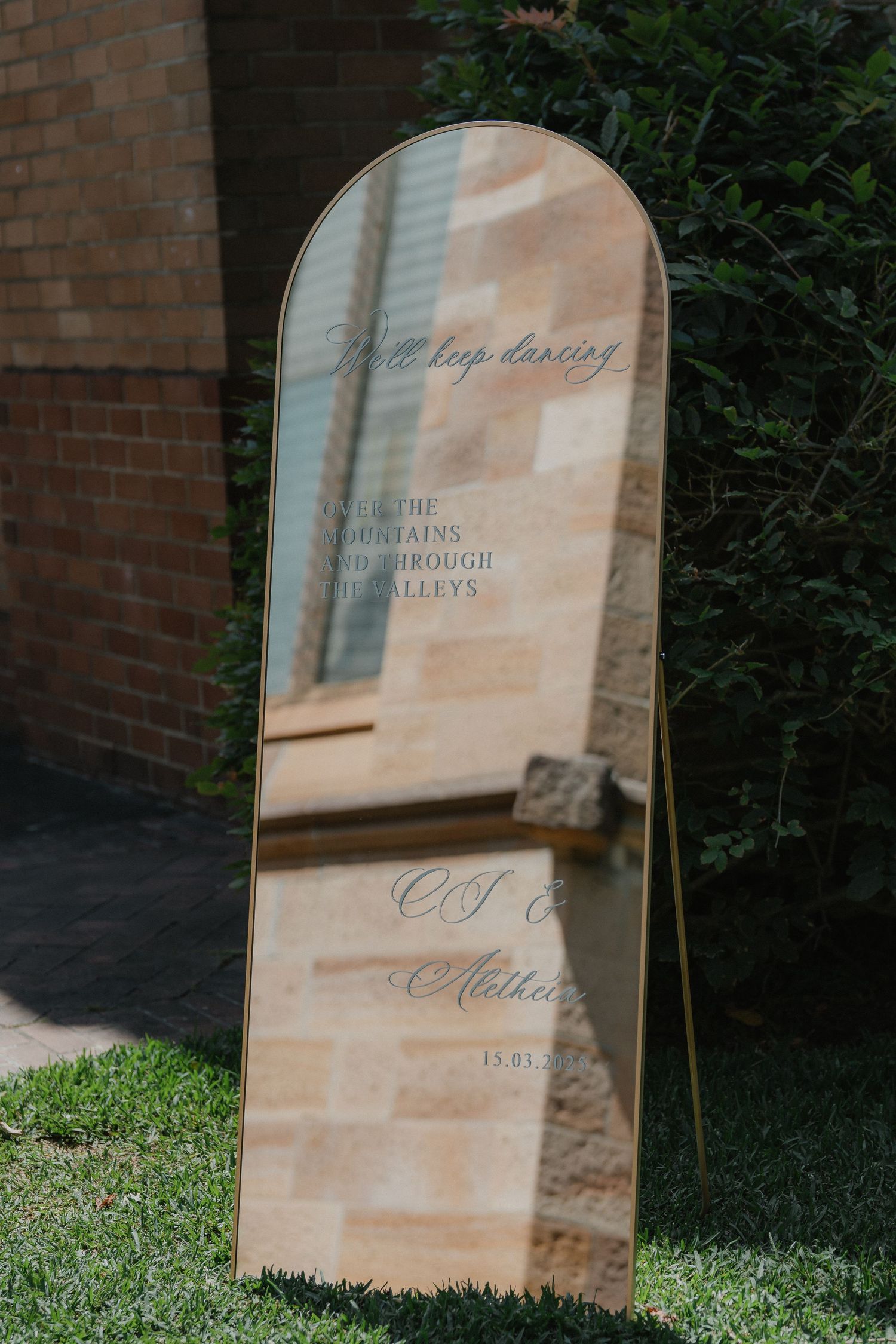 An elegant arched mirror reflects soft sunlight against a brick wall in an outdoor setting.