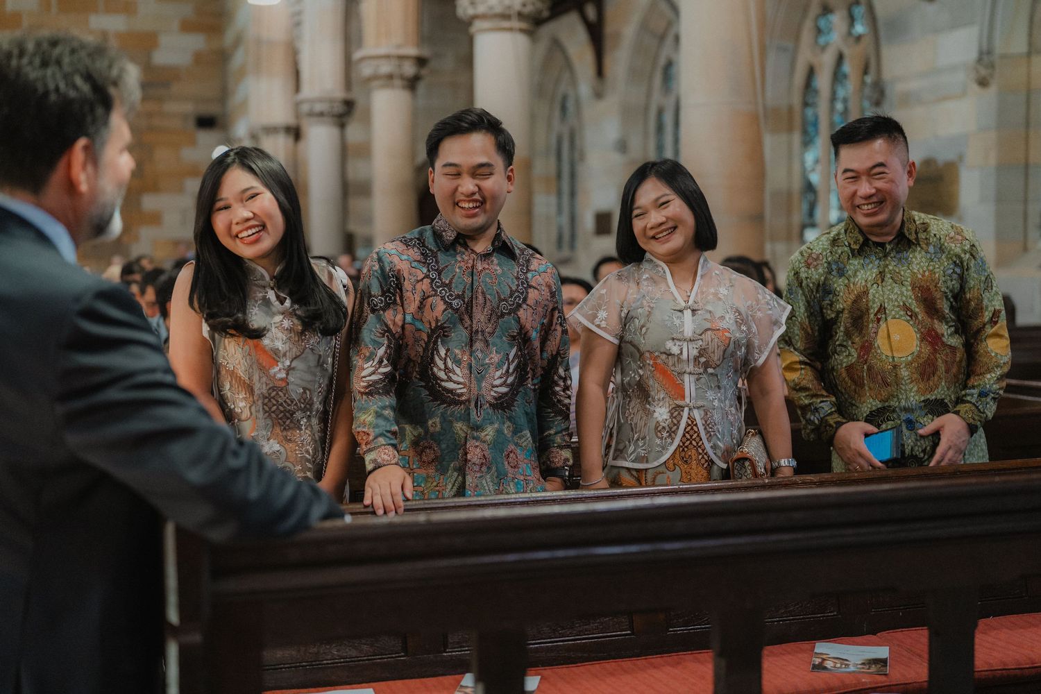 Wedding party members in traditional batik attire share joyful moments in a church setting.