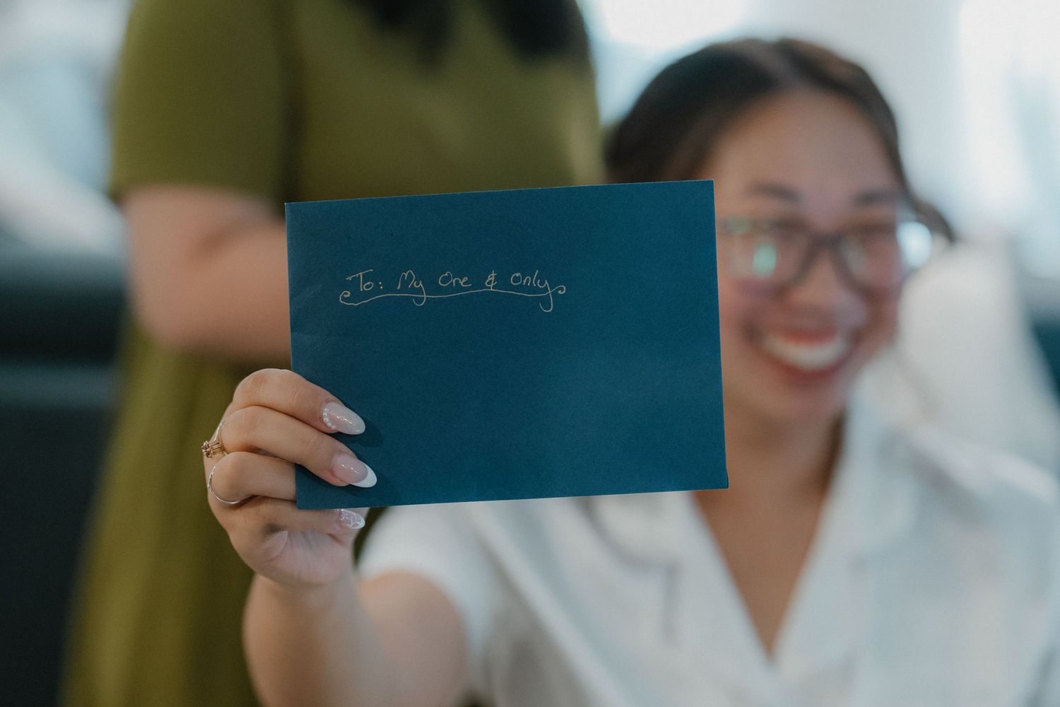 Professional handing a blue passport or document in an office setting with person in white attire in background.