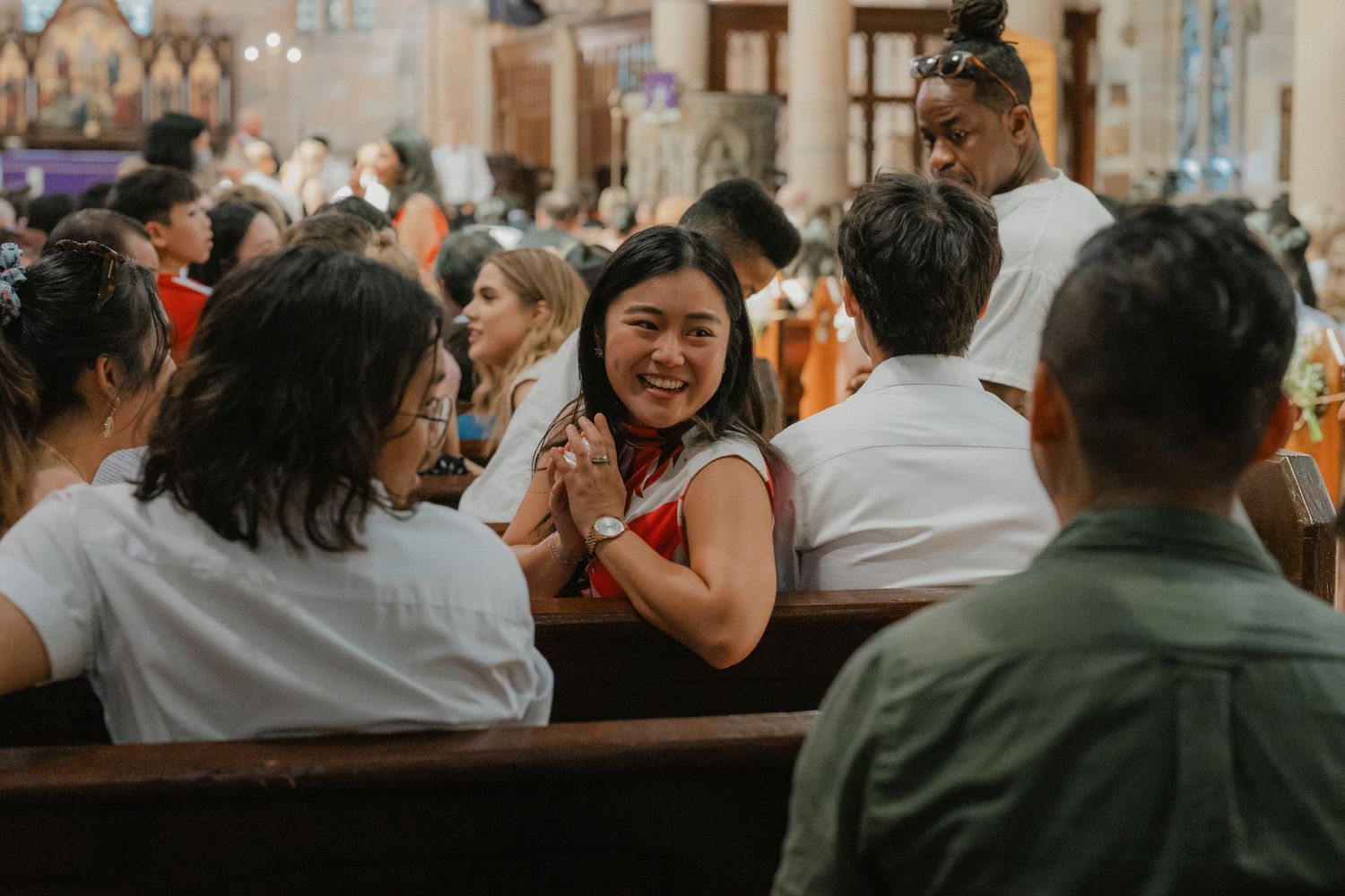 Wedding guests share joyful laughter while seated in church pews during a celebration.