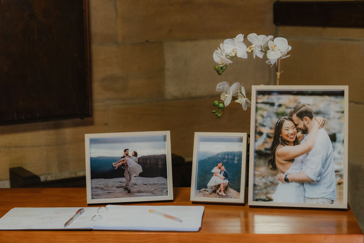 Wedding photos displayed on a wooden table with a white orchid flower in the background.