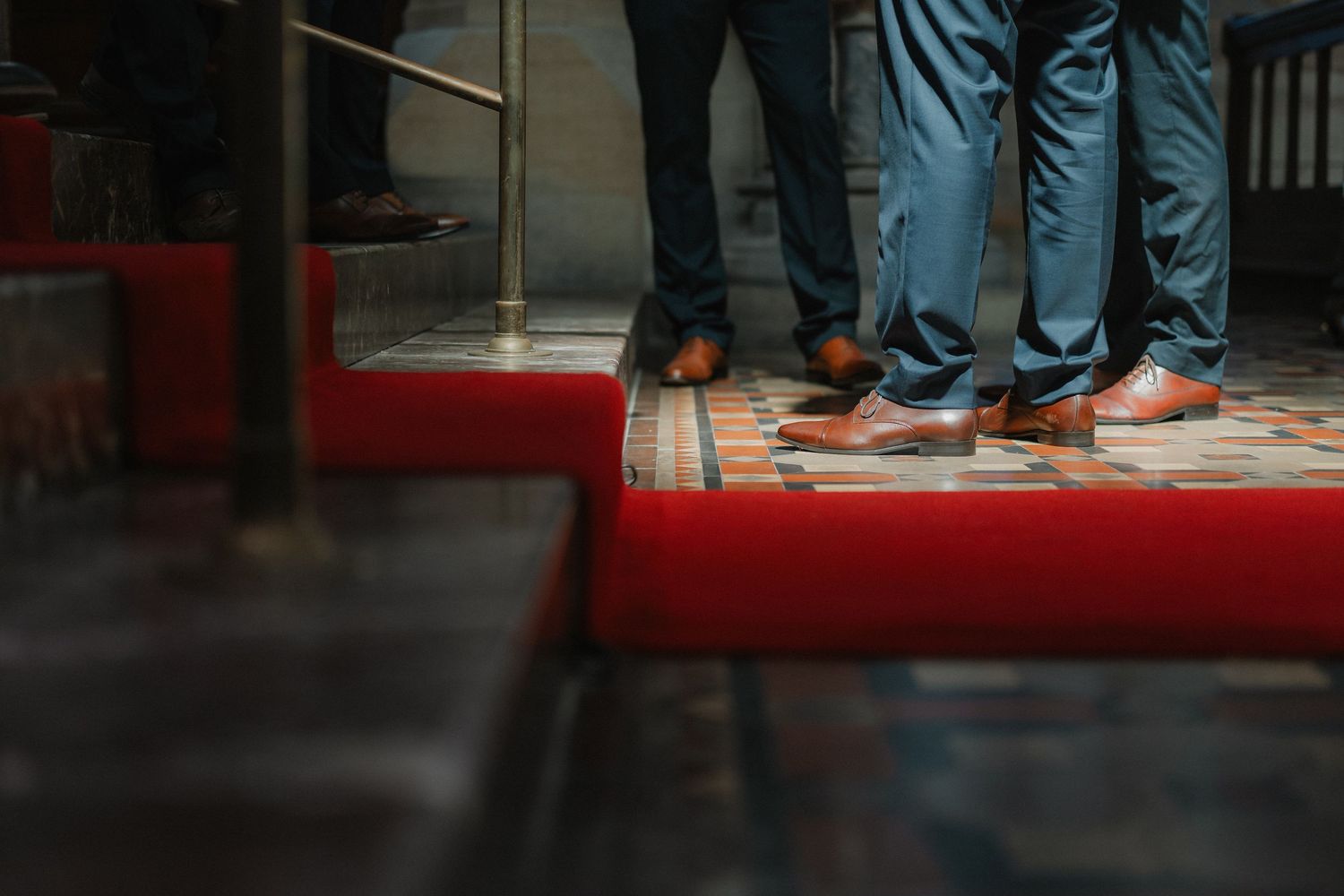 Details of formal shoes and clothing on a red carpet.