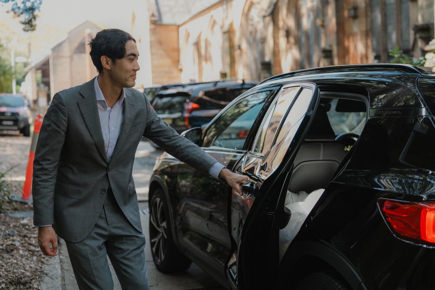 A well-dressed guest opens a car door in a parking lot outside a church.