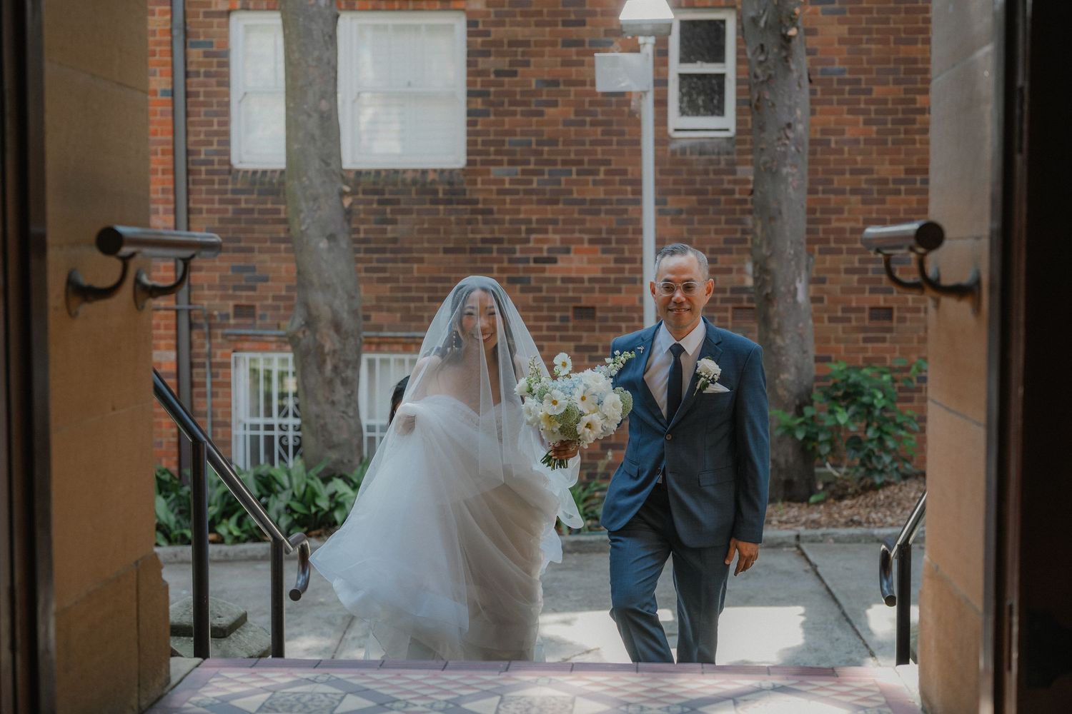 A couple enters through a brick archway on their wedding day.