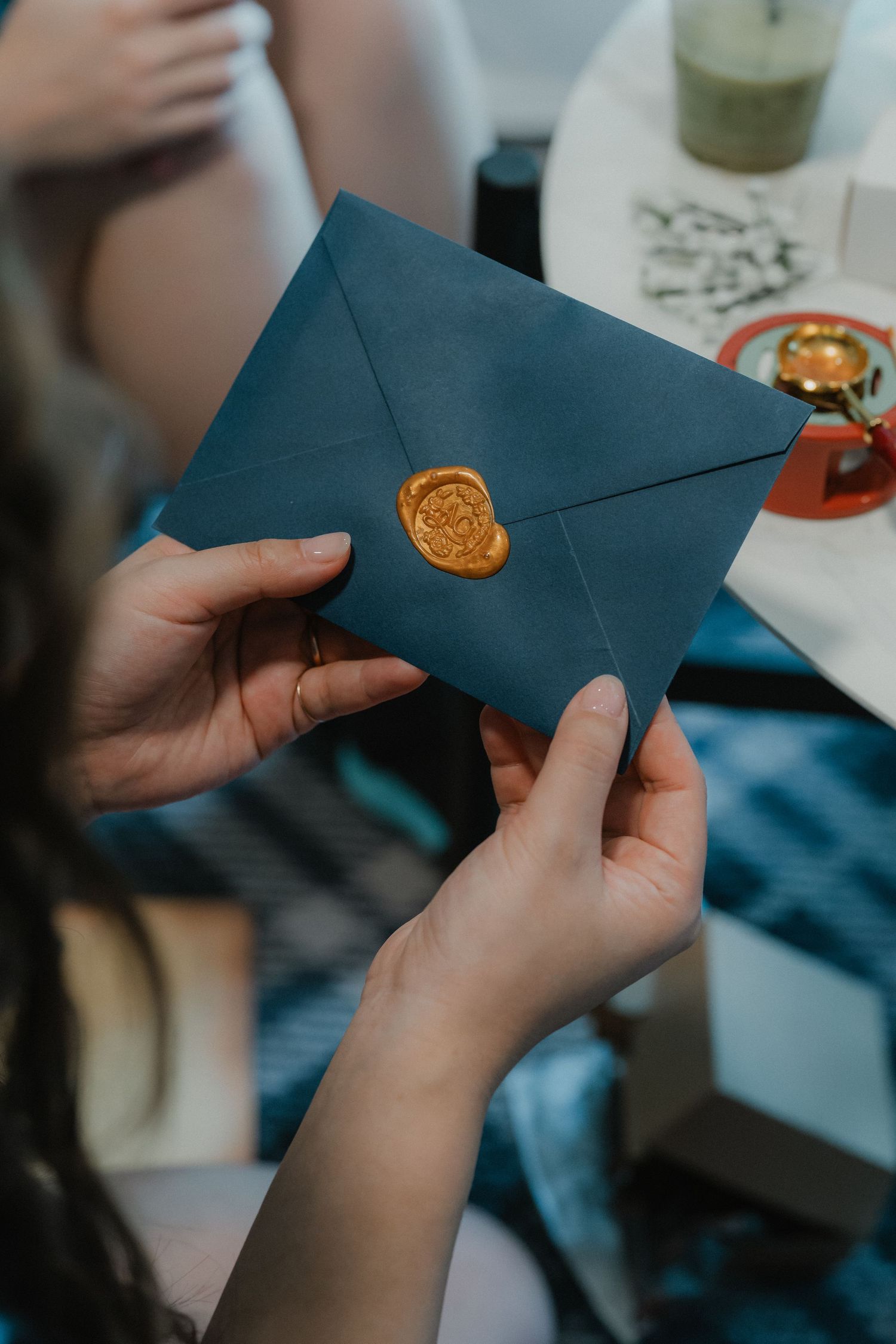 Hands opening a dark navy blue envelope with a gold wax seal, shown in sequential frames.