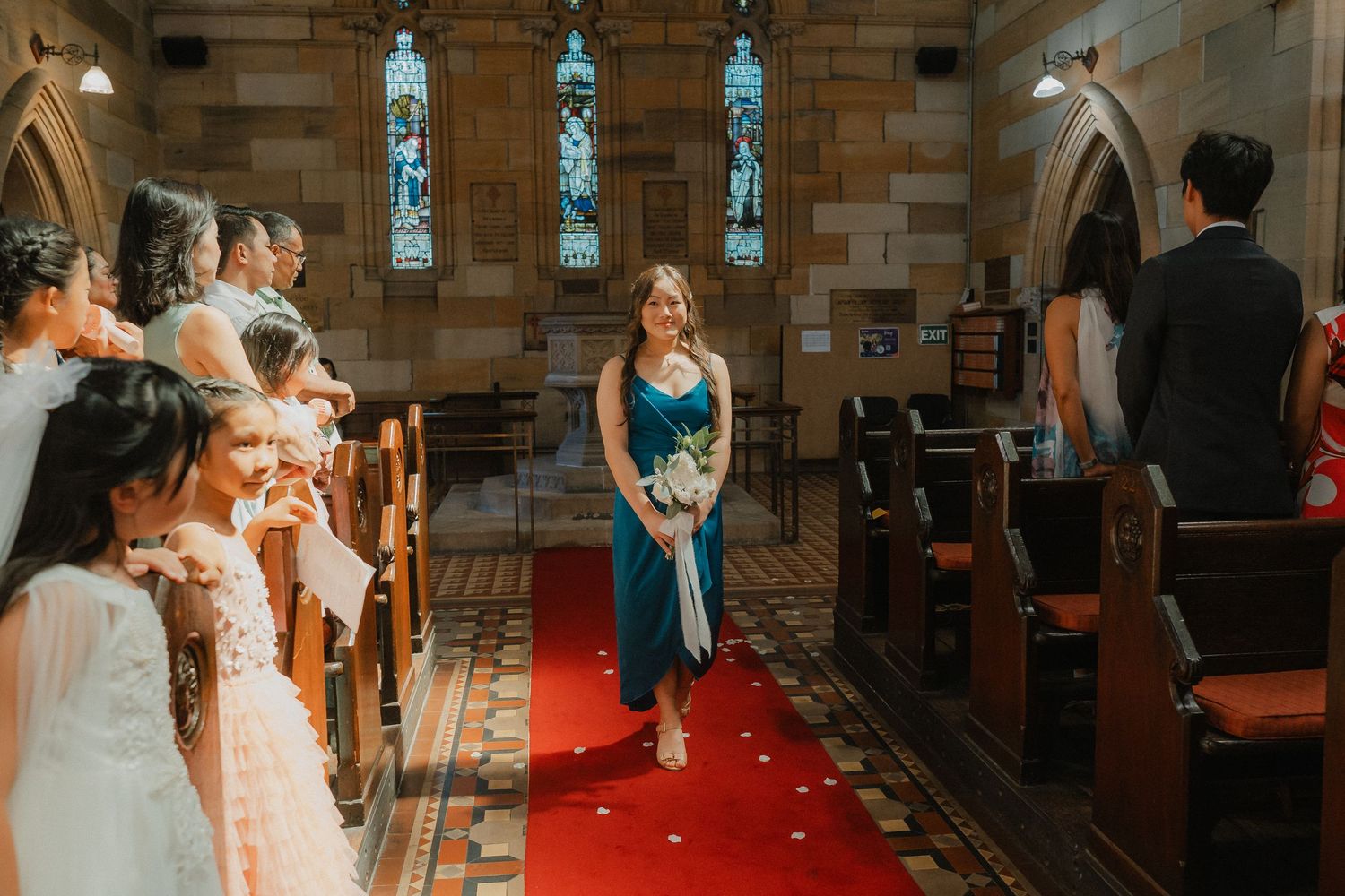 Wedding ceremony in a church with stained glass windows and a red carpet aisle at the center.