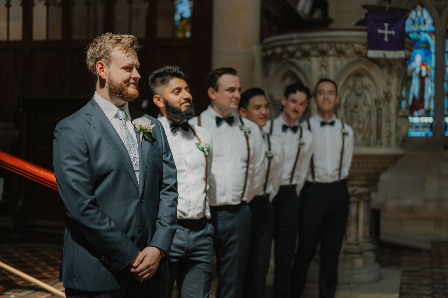 Wedding party stands at altar in traditional church with groomsmen in suspenders.