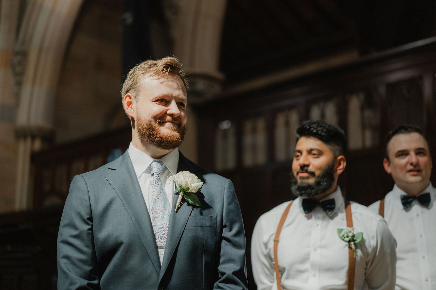 Groomsmen in suits and suspenders stand at altar during wedding ceremony.