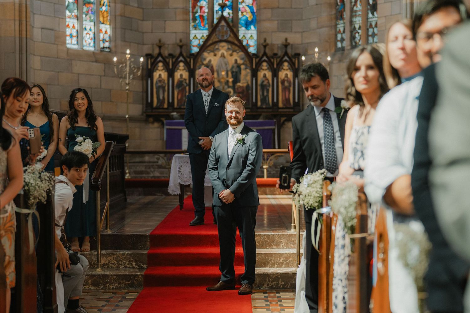 Wedding guests gather in a beautiful church cathedral with stained glass windows and gothic architecture.