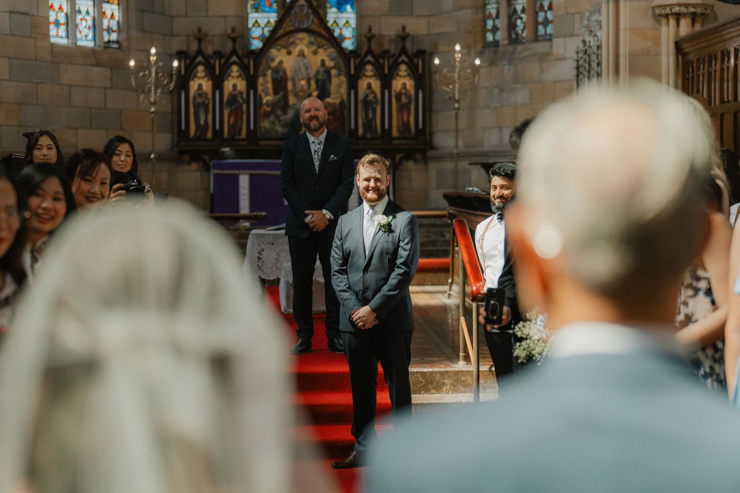 A wedding ceremony unfolds in a traditional church with ornate altar and red carpet aisle.