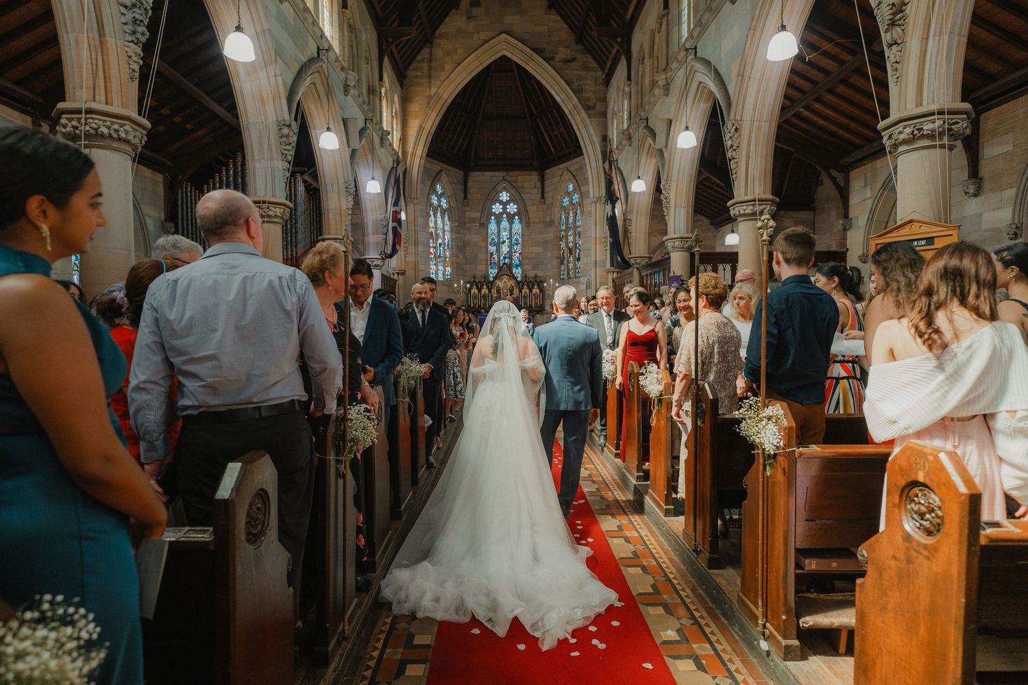 A traditional church ceremony with guests lining the pews and a red carpet runner down the aisle.